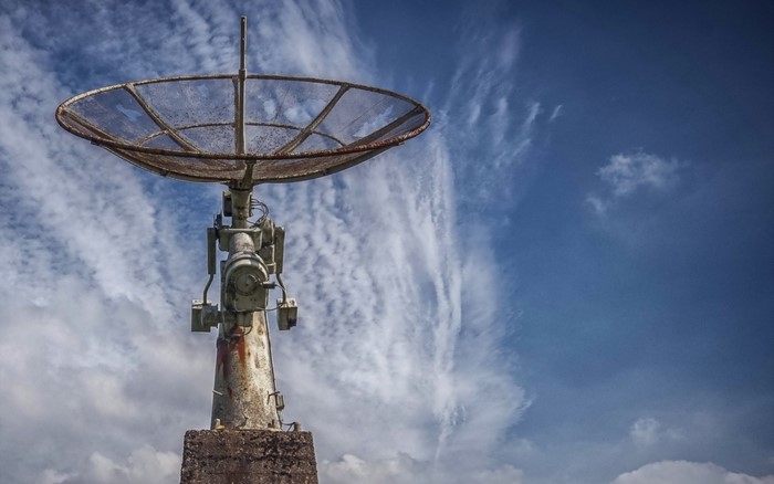 Rusty satellite dish on a concrete base against a cloudy sky