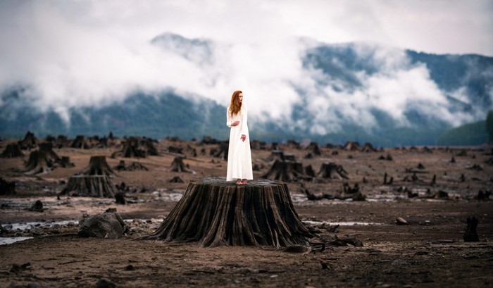 Woman in white dress standing on a tree stump in a deforested area