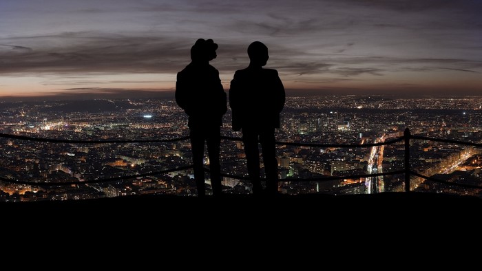 Two silhouettes overlooking a city at dusk