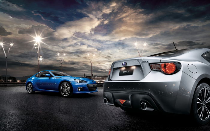 Two Subaru BRZ sports cars on a wet road at dusk