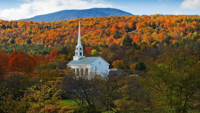 White church in autumn forest with mountains