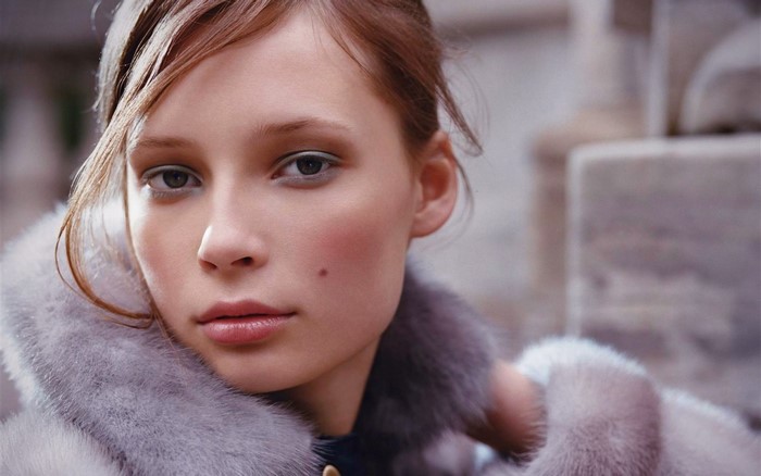 Close-up portrait of a young woman with brown hair wearing a fur coat