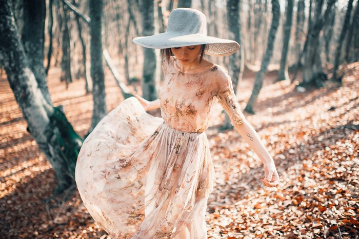 Woman in a wide-brimmed hat and floral dress in a forest