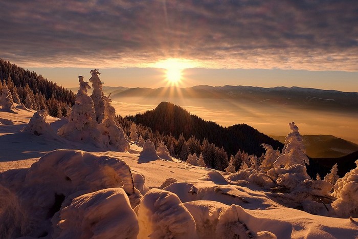 Winter sunrise over snowy mountains and forest valley