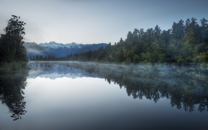Misty lake reflection of snowy mountains and forest in New Zealand