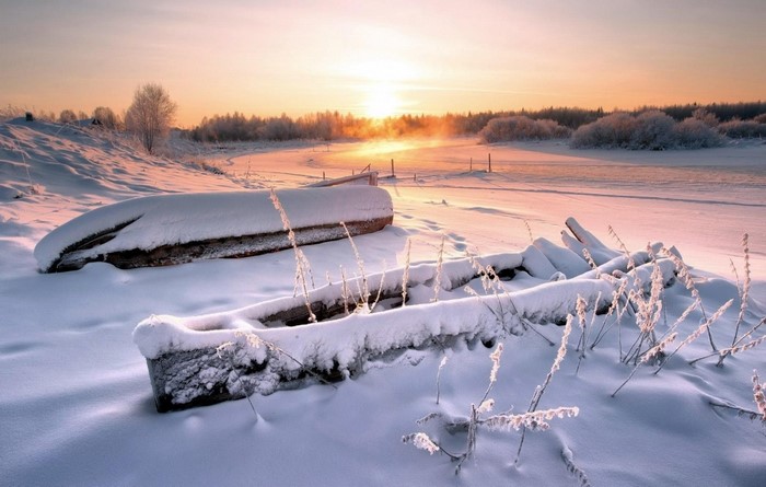 Snow-covered boats on a frozen landscape at sunrise