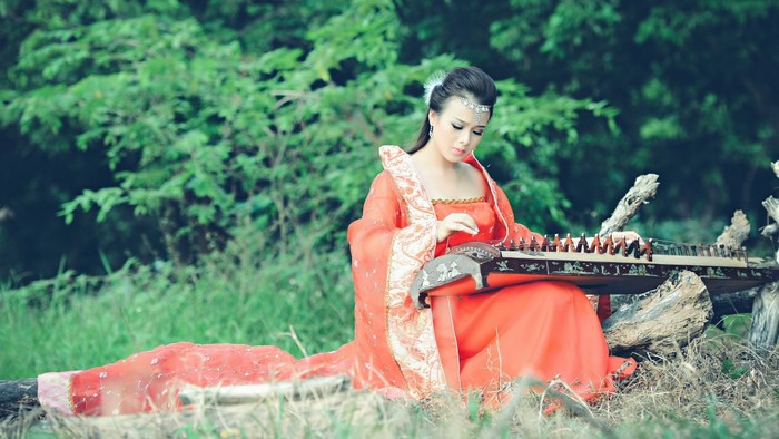 Woman in orange dress playing a string instrument in a forest