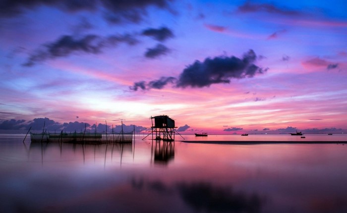 Sunset over the sea with a stilt house and fishing nets