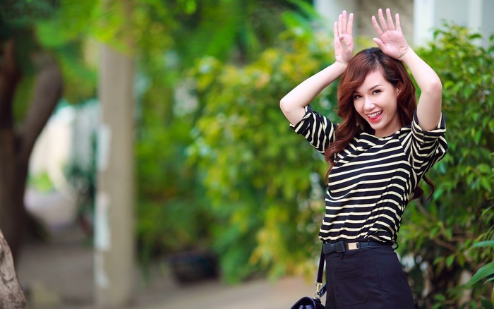 Asian woman with long brown hair wearing a striped shirt and black skirt
