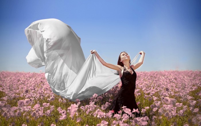 Woman in black dress holding white fabric in flower field