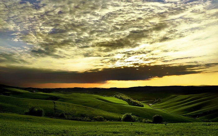 Rolling green hills under a dramatic sunset sky