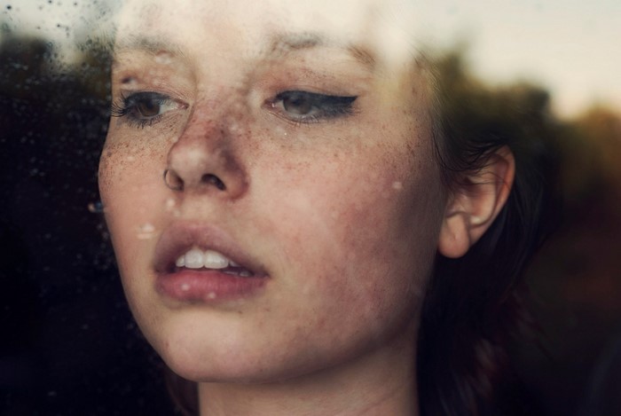 Close up of a young woman with freckles looking out a window