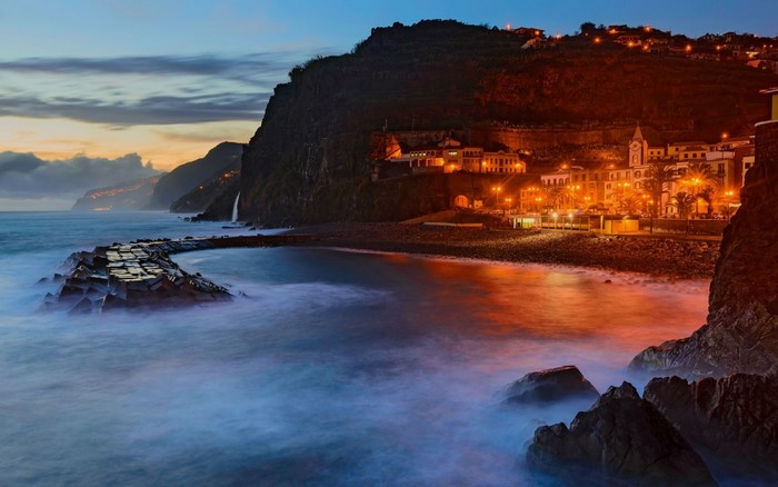 Coastal town at dusk with ocean waves and cliffs