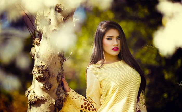 Woman in yellow dress posing by a tree