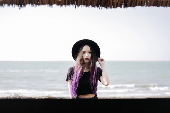 Woman with purple hair and black hat at the beach