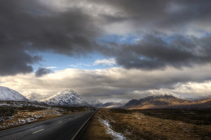 Road through snowy mountains in Scotland under dramatic clouds