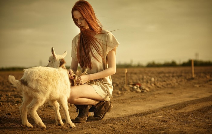 Redhead woman with goat in a field