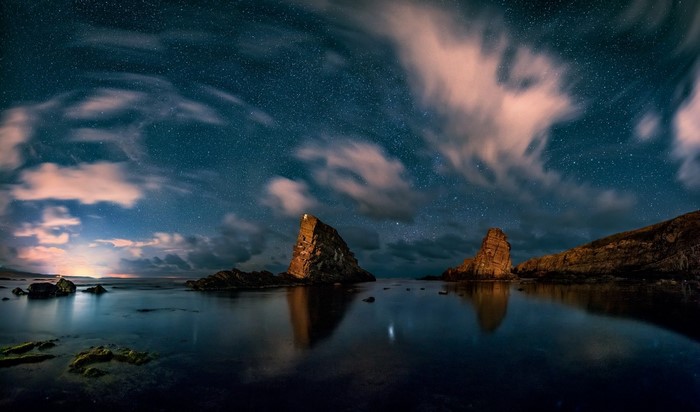 Starry night over rocky coast with ocean reflection