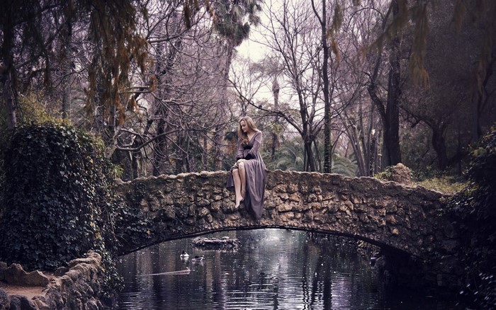 Woman sitting on a stone bridge over water in a forest