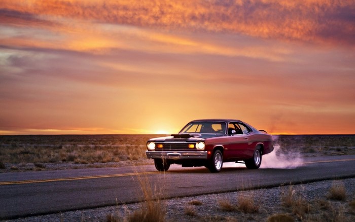 Red Dodge Duster driving on a road at sunset