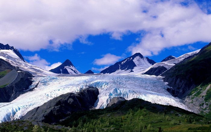 Glacier flowing between snow-capped mountains under a blue sky