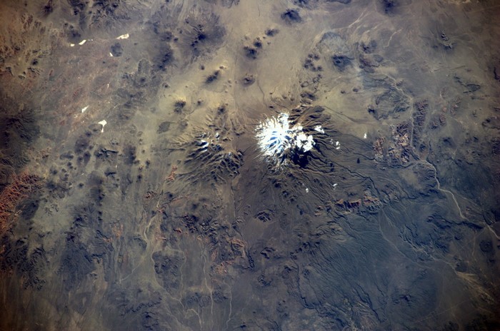 Snow-capped volcano in a barren landscape from space