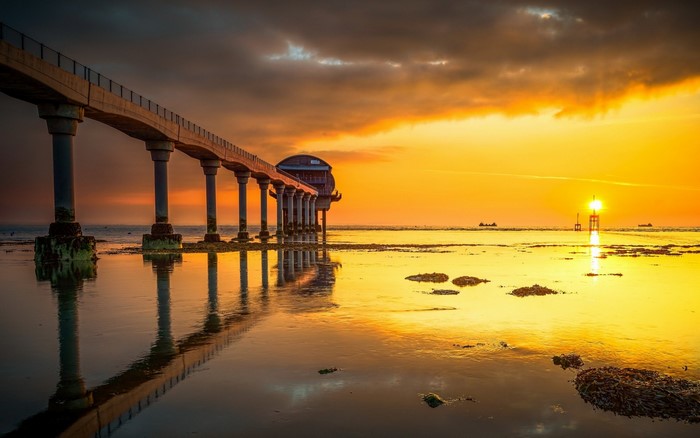 Pier and lighthouse at sunset over the ocean