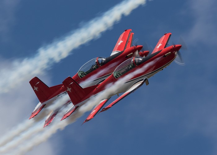 Four red and white Pilatus PC-7 aircraft performing aerobatics