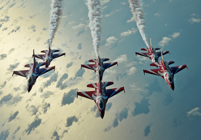 Five fighter jets performing aerobatics with smoke trails