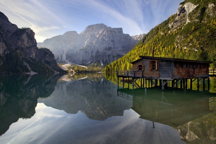 Wooden cabin on a lake with mountains and forest reflection
