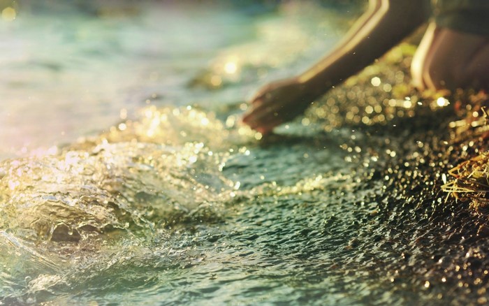 Person's hand touching shallow water with sunlight reflections