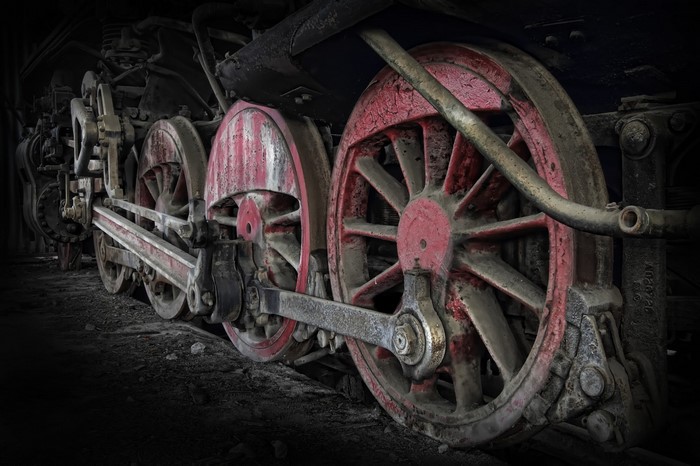 Close-up of a weathered steam locomotive's red wheels and machinery
