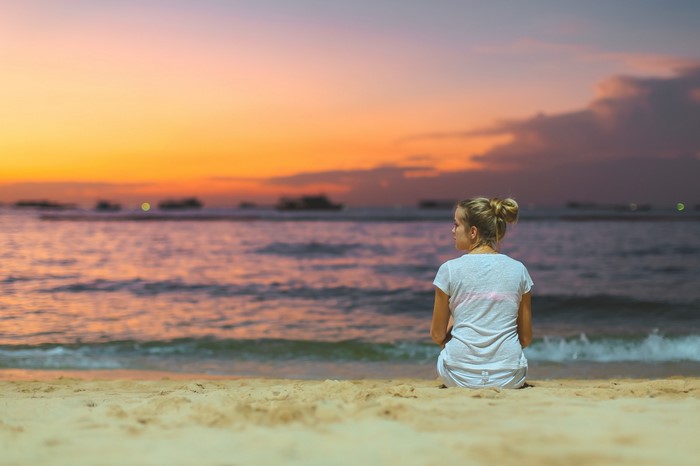 Woman sitting on a beach at sunset