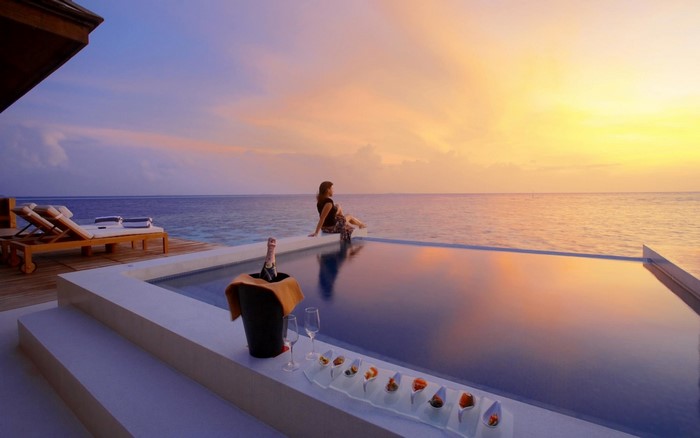 Woman by infinity pool at sunset with champagne and appetizers