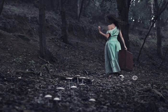 Woman in green dress carrying suitcase in dark forest