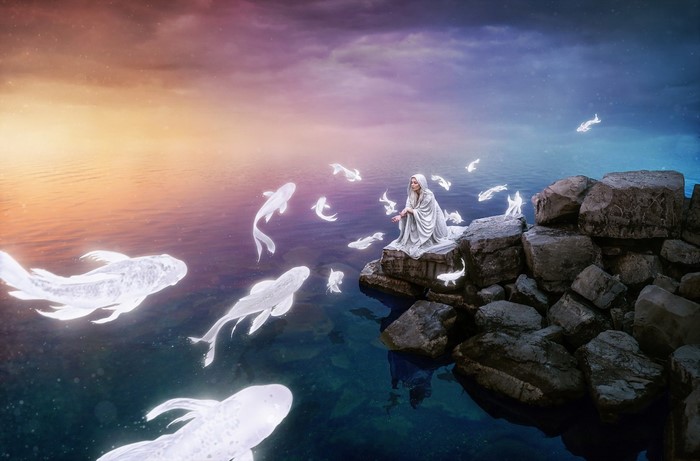 Woman in white robe with glowing fish by the sea