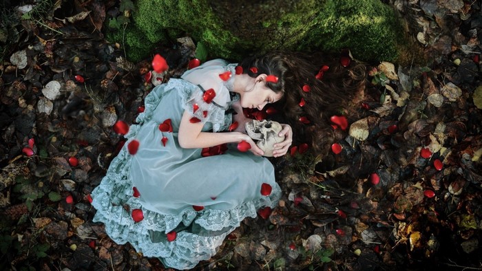 Woman in dress holding a skull surrounded by rose petals