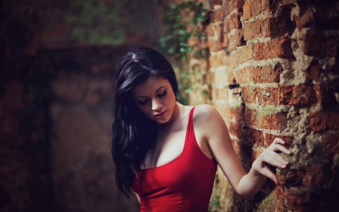 Woman in red dress leaning against a brick wall