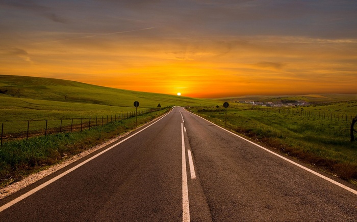 Road through green hills at sunset