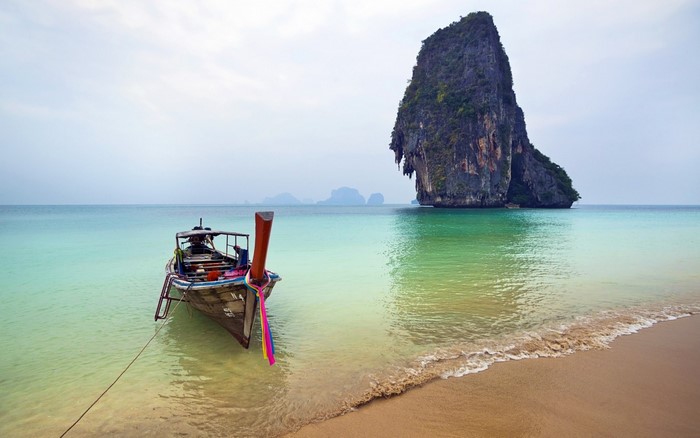 Longtail boat on a tropical beach with a large rock island