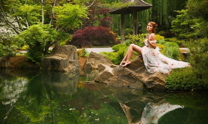 Woman in a floral dress sitting on rocks by a pond in a garden