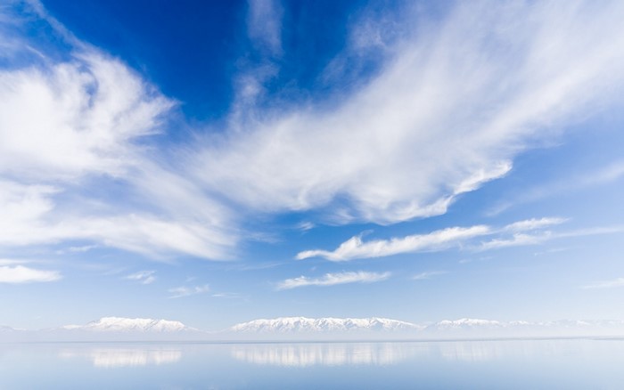 Snow-capped mountains reflected in a calm body of water under a cloudy sky