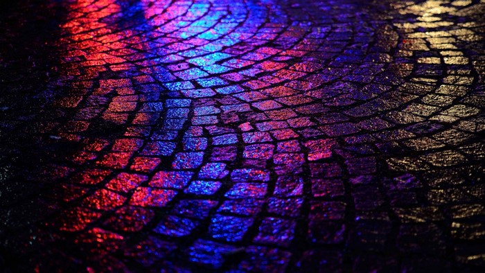 Colorful reflections on wet cobblestone pavement at night