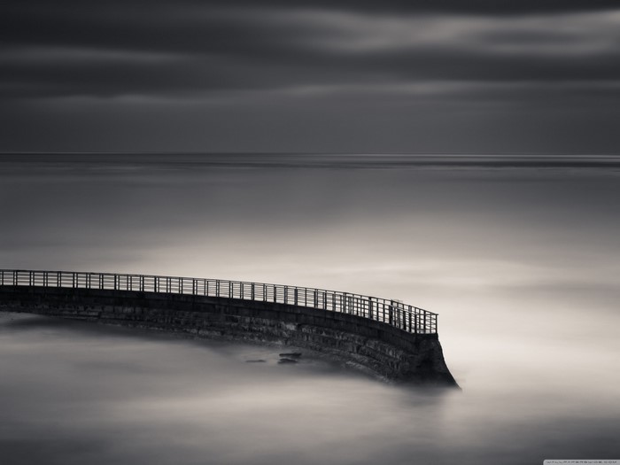 Monochrome view of a curved pier over misty ocean at dawn
