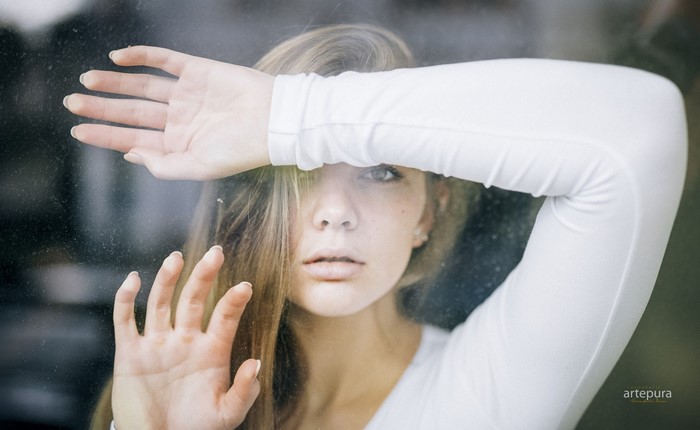 Woman with hand over face looking through window