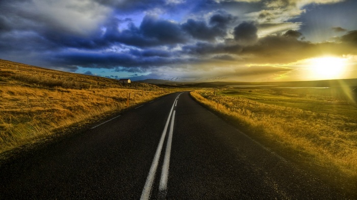 Road through a grassy landscape at sunset