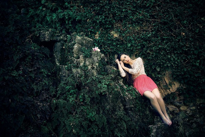 Woman lying on mossy rocks with a flower