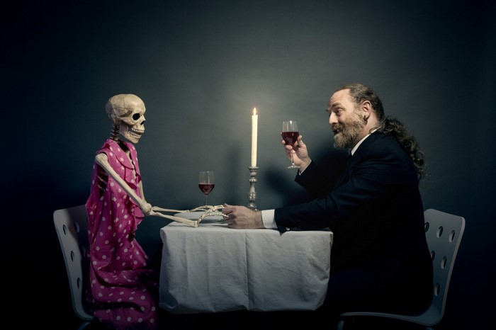 Man and skeleton having dinner with wine