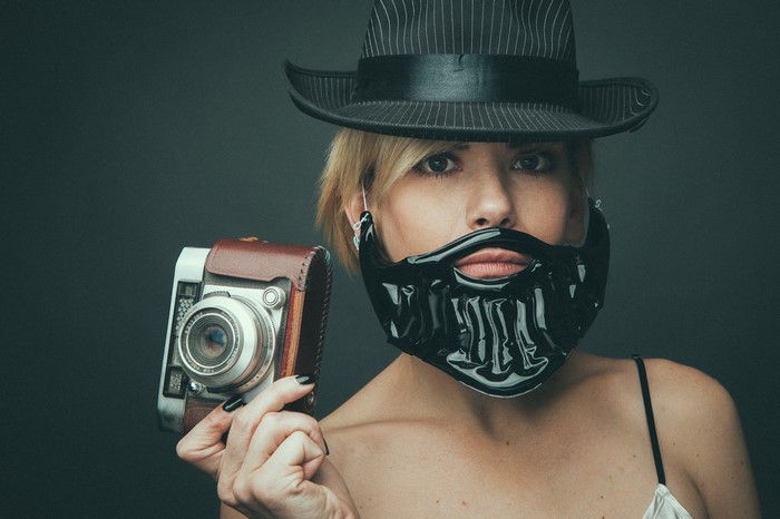 Woman in hat and fake beard holding vintage camera