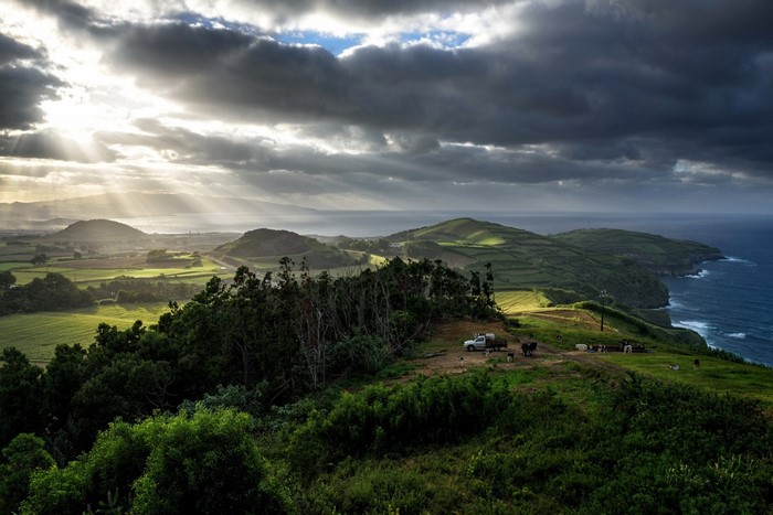 Sunlight breaking through clouds over coastal hills and sea